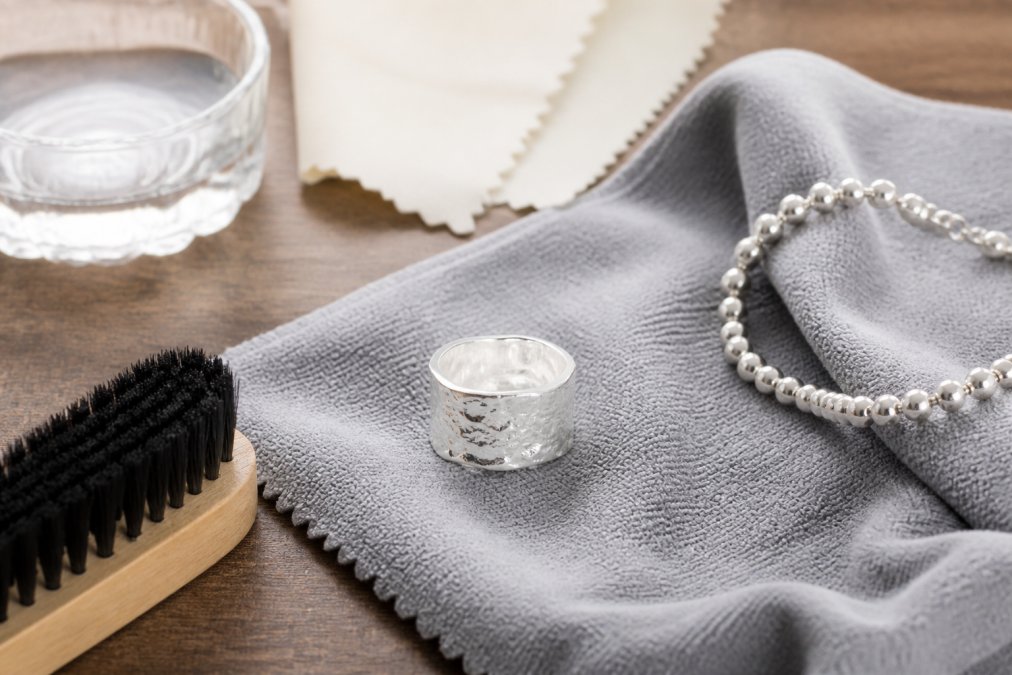 Handcrafted silver jewelry pieces displayed on soft cloth with polishing materials, microfibre cloth, and gentle cleaning tools nearby, demonstrating proper care and maintenance