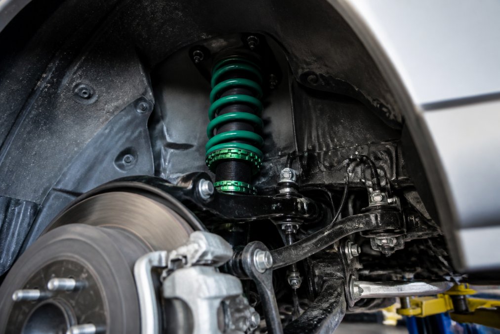 Close-up of a Subaru suspension system showing coilover assembly, shock absorbers, and spring components mounted in a clean workshop environment under bright diagnostic lighting