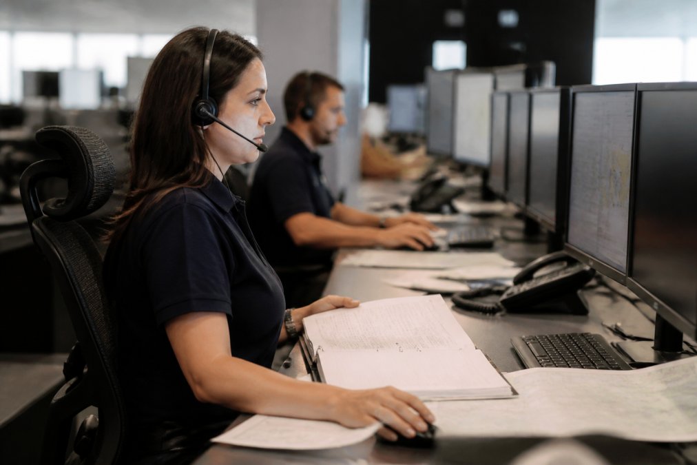 Female aircraft dispatcher wearing a headset reviewing flight plans on monitors in a modern operations center