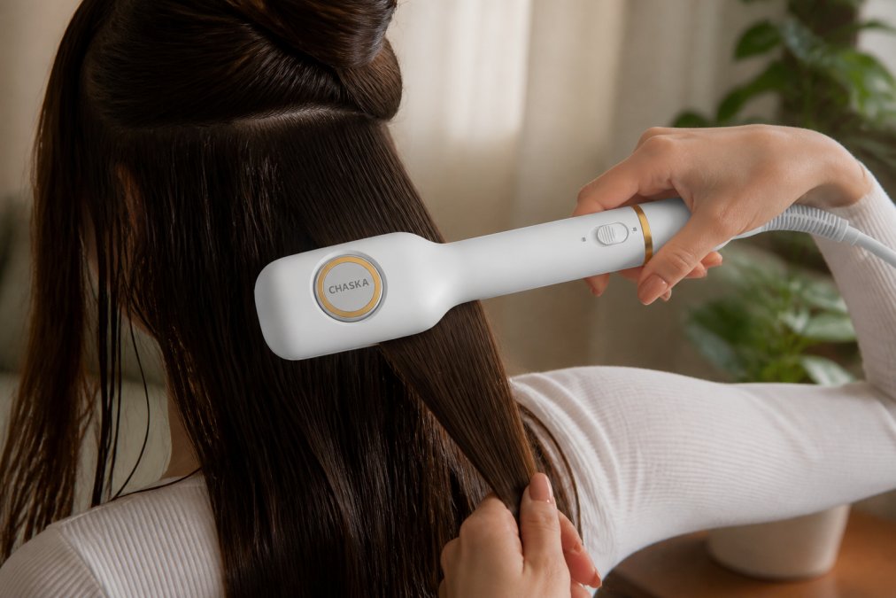 Close-up of hands demonstrating proper grip and technique while using an all-in-one styler on damp hair, with natural lighting showing the straightening and curling motions