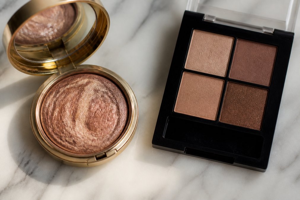 Side-by-side flat lay of a luxury artisanal makeup compact with visible pigment texture next to a standard mass-produced plastic palette, on a marble surface with soft natural lighting