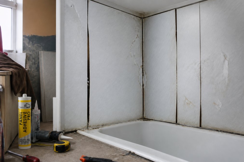 A poorly installed bathroom panel showing visible gaps between panels, uneven alignment, and moisture damage visible around the edges and seams, demonstrating what to avoid
