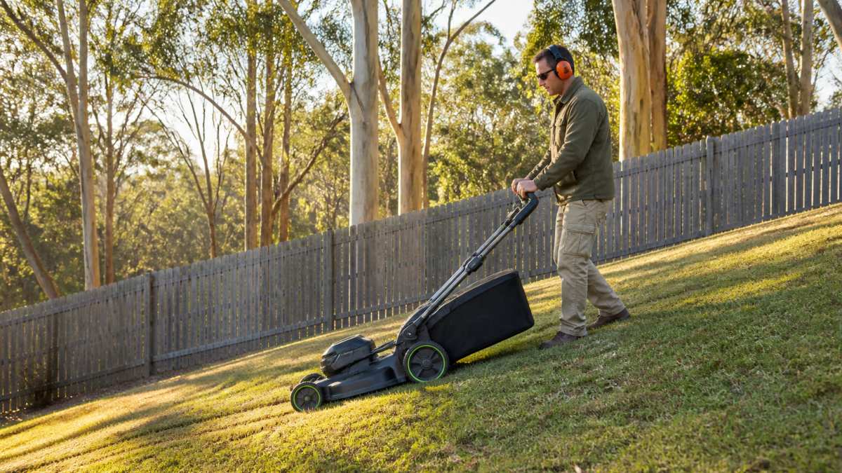 Person mowing a sloping residential lawn with a quiet battery powered lawn mower at sunrise