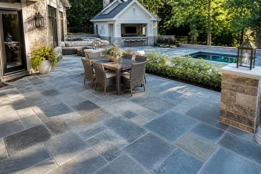 Finished bluestone patio with natural cleft surface on a luxury residential property, showing blue-gray tones and varied texture in natural daylight, with landscaping and home in background