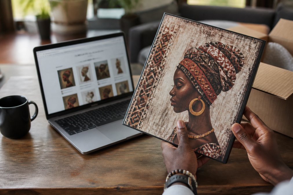 Hands comparing black heritage decor art prints against online store listings on a laptop screen