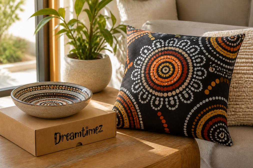 A warm, styled living room scene featuring an Indigenous-designed cushion and ceramic bowl on a timber coffee table, with soft natural light streaming through a nearby window
