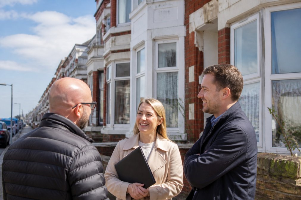 A row of traditional Victorian terraced houses in Blackpool, some displaying letting agent boards, under a bright coastal sky