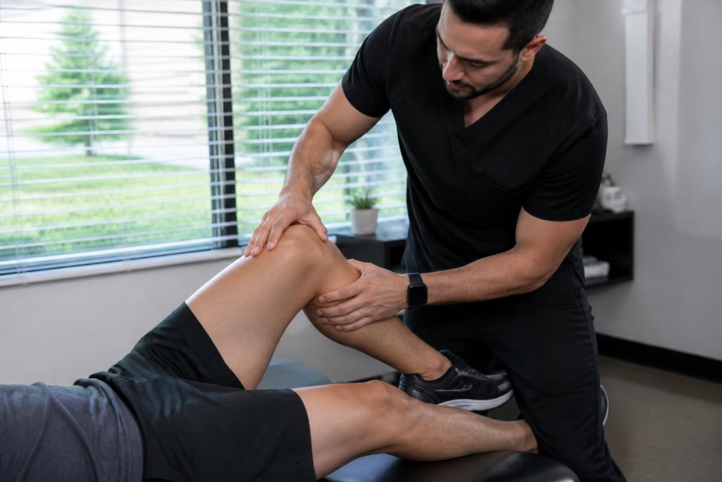 A chiropractor in a modern San Antonio clinic gently assessing a runner's knee alignment on a treatment table, with the patient lying comfortably and natural lighting through window blinds