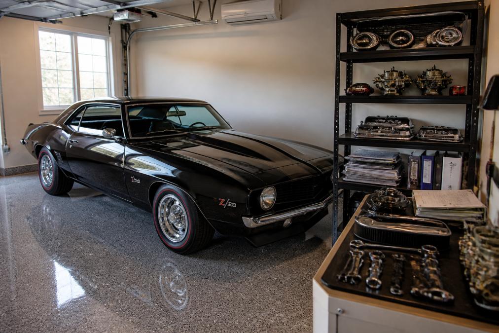 Muscle car parked in a climate-controlled garage with proper storage setup, showing maintenance tools, original parts, and documentation organized on shelves nearby, with soft natural light from garage windows