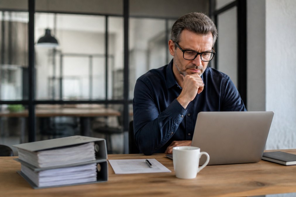 Consultant reviewing client project details on a computer at a desk with organized files and a cup of coffee nearby