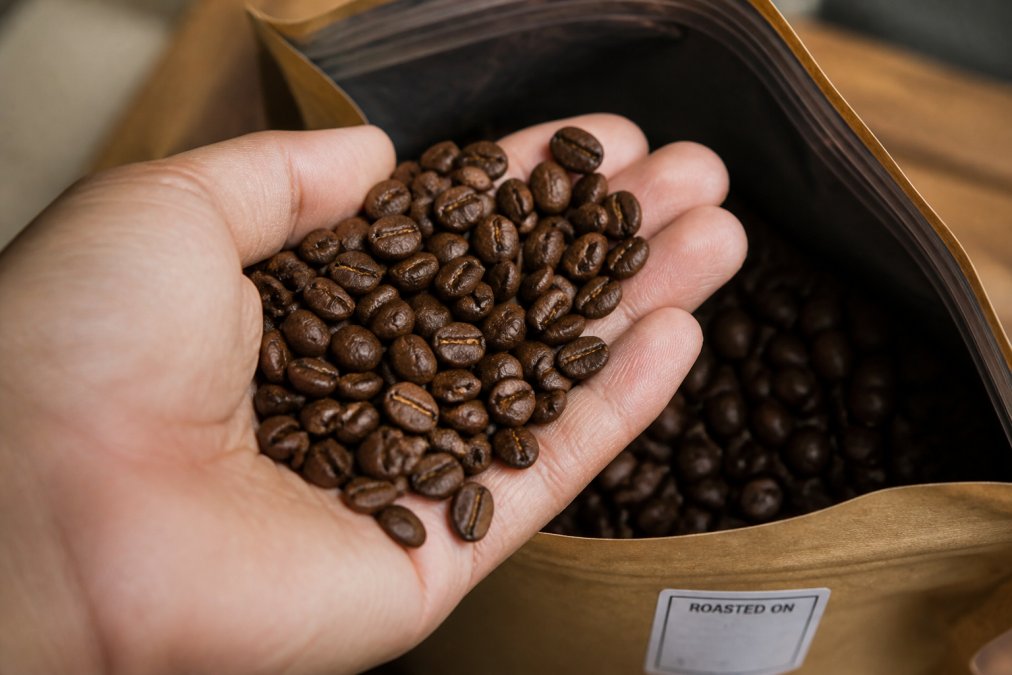 Close-up of freshly roasted whole bean coffee in a hand, showing rich color and aroma, with roast date label visible