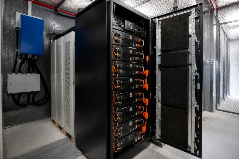 Close-up view of industrial battery energy storage system units installed in a secure facility room, showing modular lithium-ion battery cabinets with electrical connections and monitoring equipment for commercial energy storage