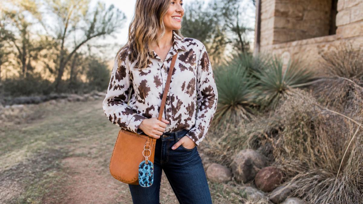 Woman wearing a cow print blouse and jeans with a leather bag and boots
