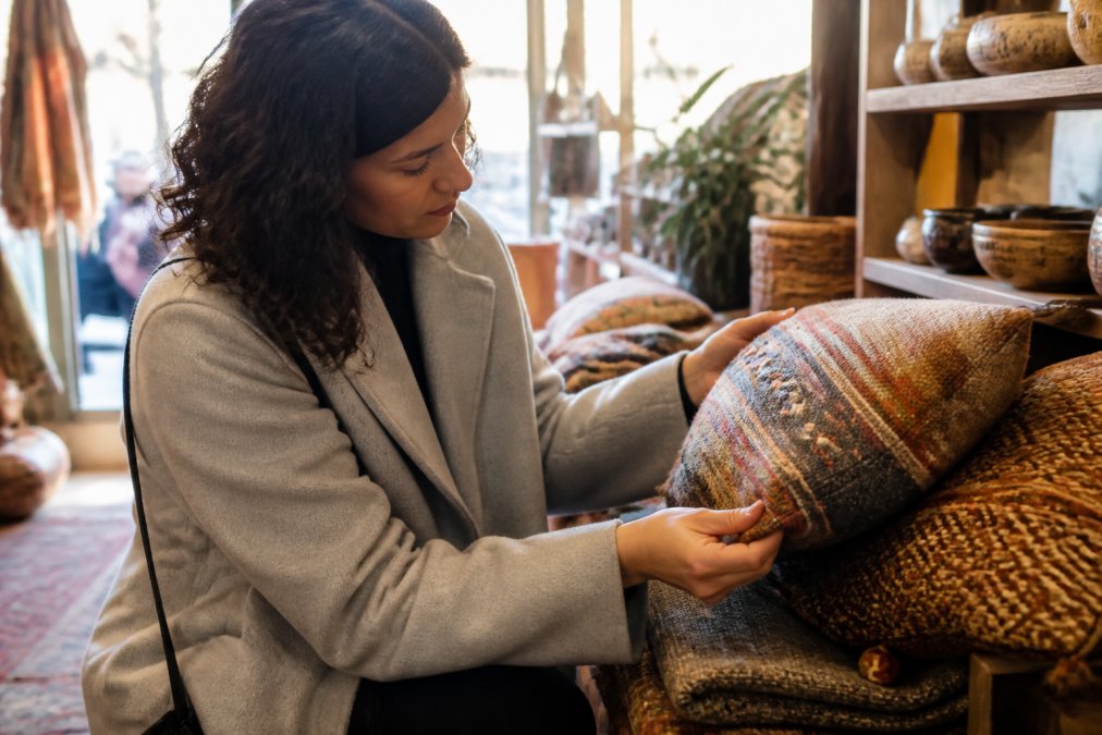 A person examining handcrafted textile details on a vintage home decor item at a boutique market, natural sunlight highlighting the quality of materials and craftsmanship