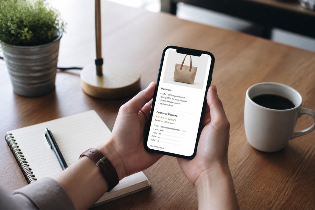Hands holding a smartphone showing product reviews for curated shopping on a desk with coffee and a notebook