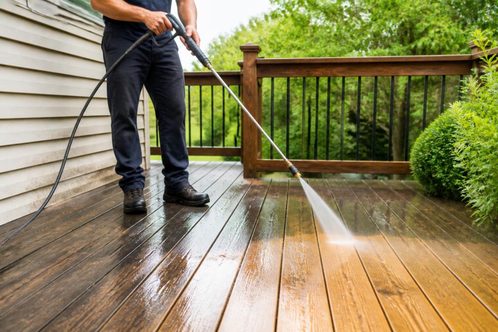Professional demonstrating pressure washing a wooden deck surface, showing water spray and cleaned wood grain becoming visible