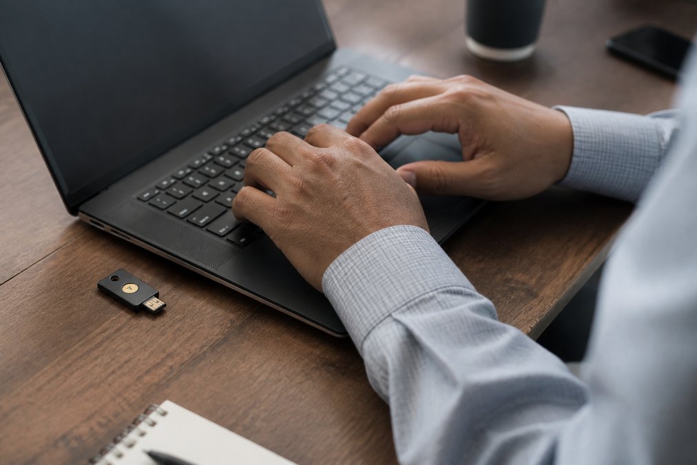 Close-up of hands typing a password on a laptop keyboard with a security key device nearby, representing secure multi-factor authentication and protected account access