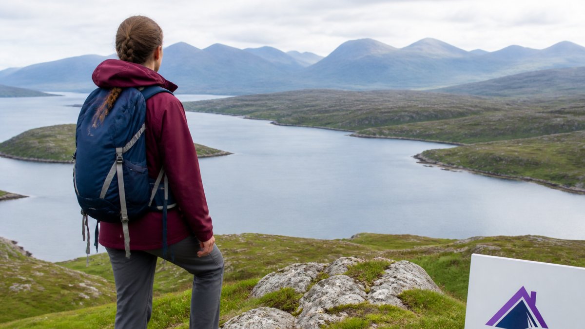 Hiker standing on a hillside overlooking Loch Dunvegan with mountain views in the distance, showcasing the scenic coastal landscape and walking routes