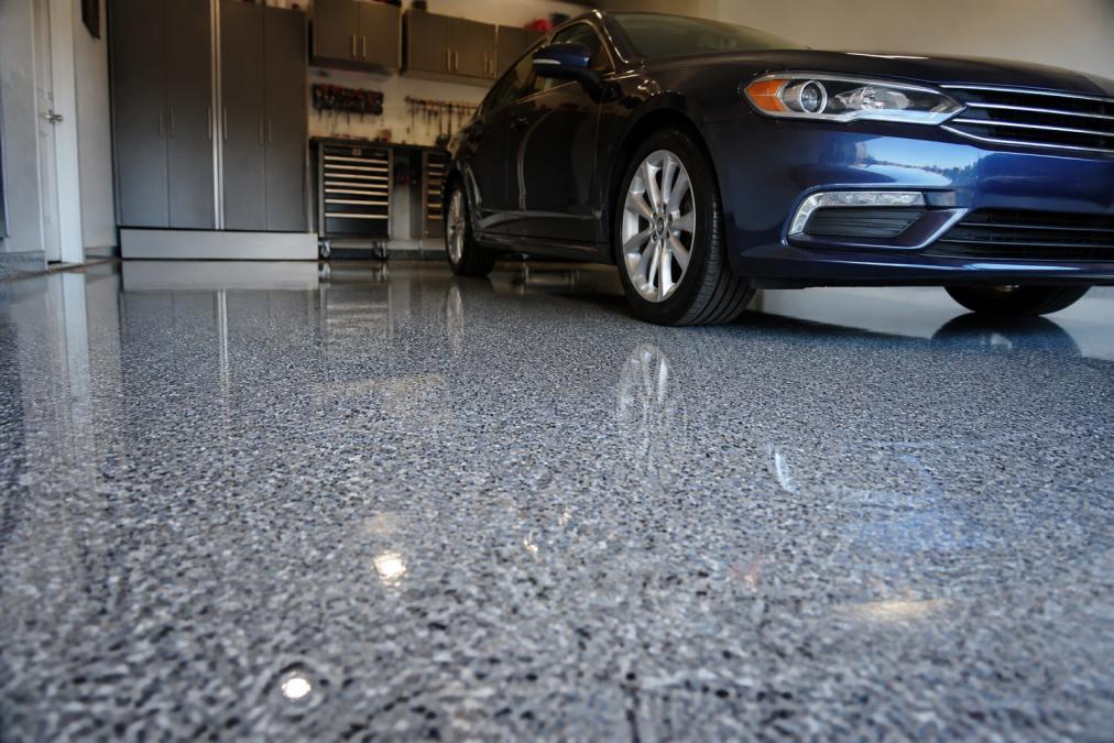 A finished residential garage floor with glossy epoxy coating displaying vibrant color flakes and polished surface reflecting overhead lighting, with a clean sedan parked on it