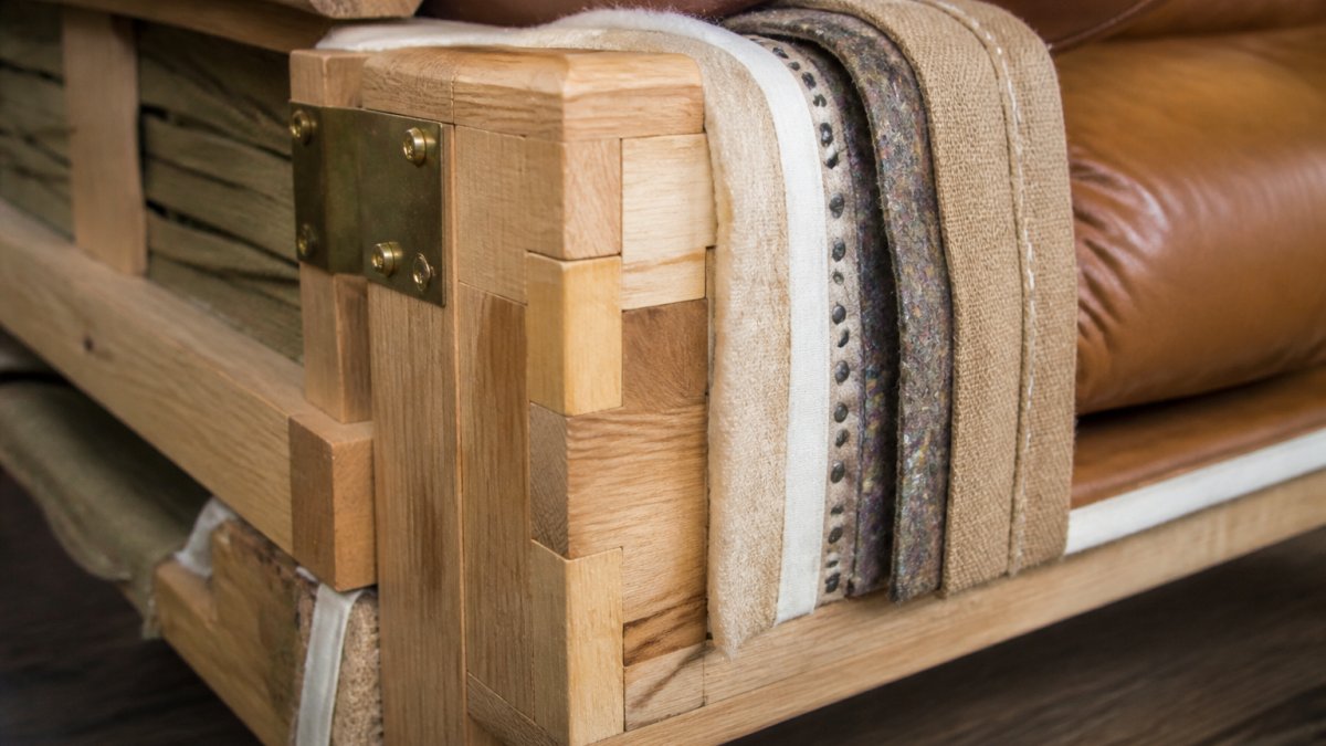 Close-up of sofa frame showing solid wood mortise-and-tenon joinery, upholstery stitching detail through multiple layers, and brass hardware attachment points