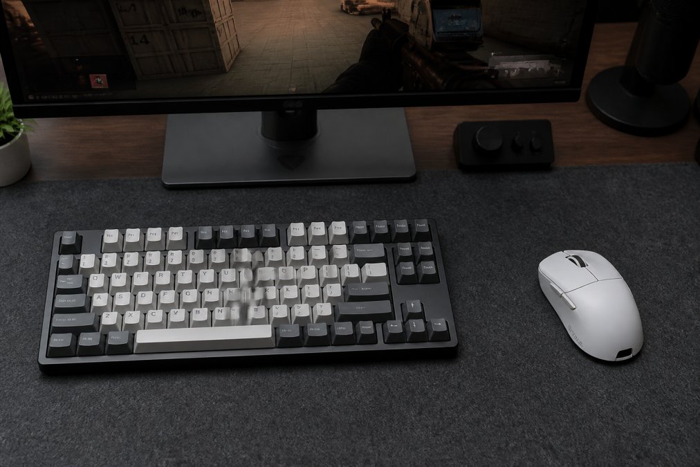 Overhead shot of a gaming desk setup with a premium mechanical keyboard, high-DPI mouse, and monitor displaying a competitive game, showing the aesthetic and tactile elements of a pro-level setup