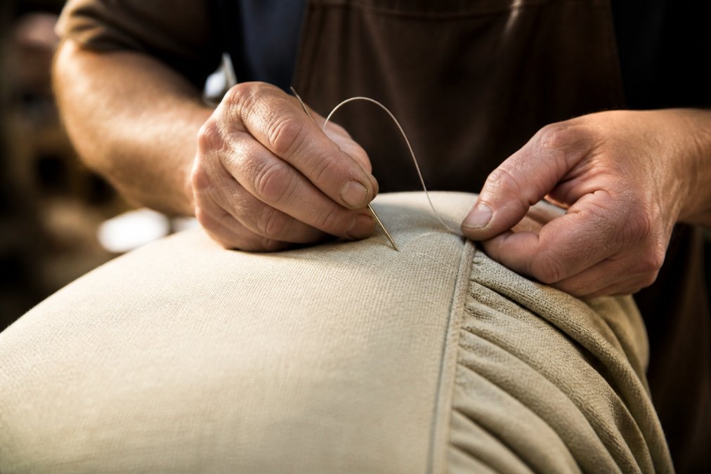 Close-up of skilled craftsperson's hands stitching high-quality upholstery with precision, showing detailed seams and premium fabric texture under warm studio lighting