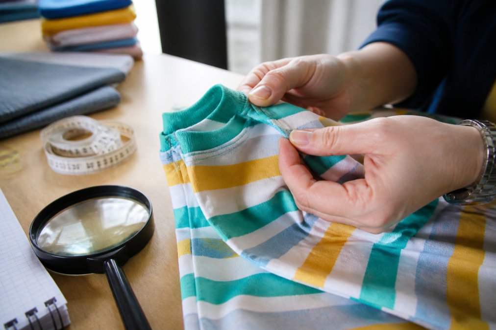 Parent inspecting the stitching and fabric of a colorful cotton t-shirt with a magnifying glass