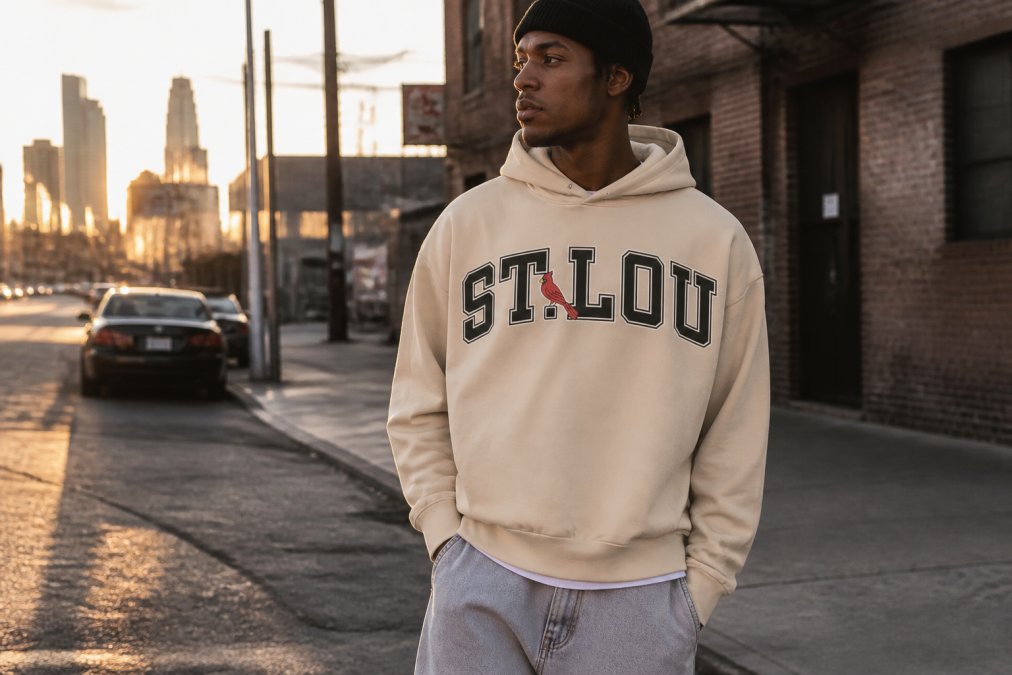 Urban tastemaker wearing a structured boxy tee layered with a brushed fleece hoodie in an authentic city street setting during golden hour, demonstrating how quality streetwear fits, moves, and drapes on the body