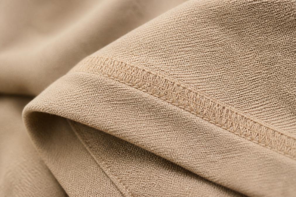 Close-up of fabric texture showing seam stitching quality, thread density, and weave pattern on a folded garment with natural lighting