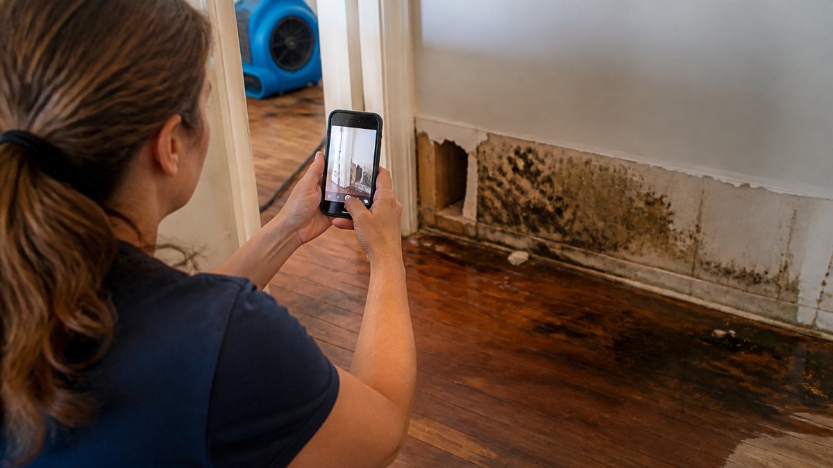 Homeowner using a smartphone to document water damage for a homeowners insurance claim on walls and flooring