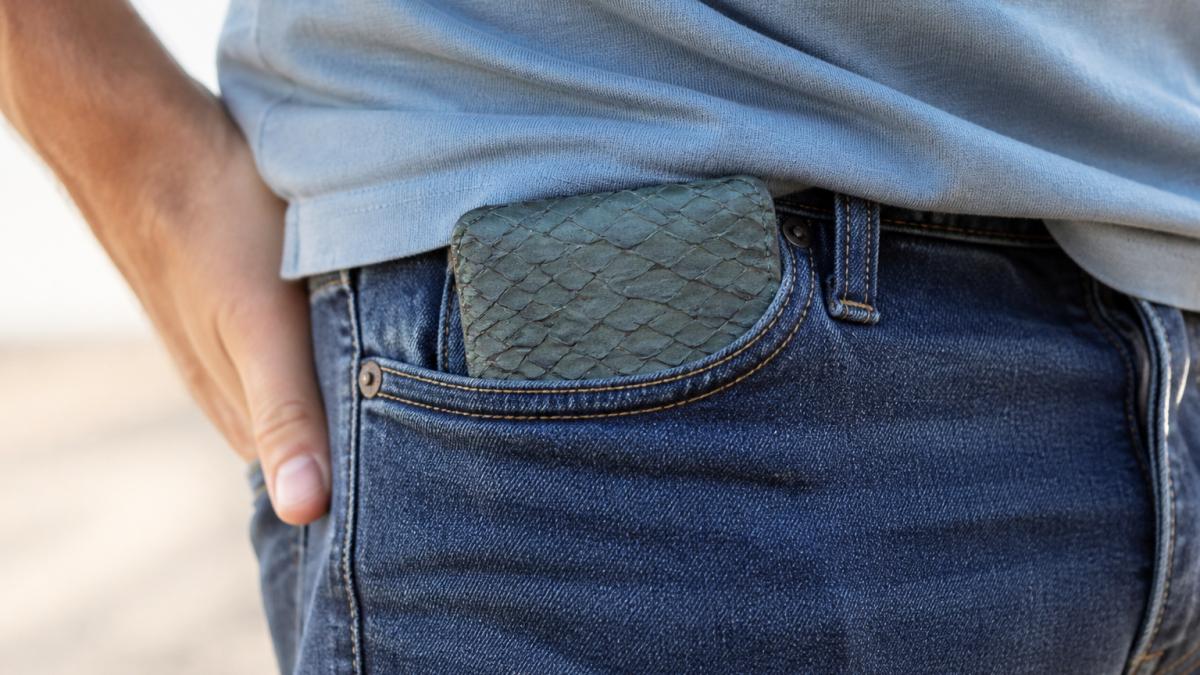 Close-up of a fish leather wallet in someone's front pocket during everyday use, showing the distinctive scale texture and color in natural daylight