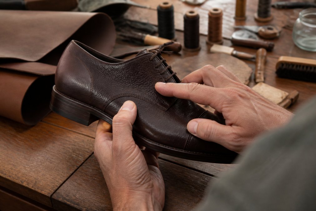 Fingers tracing the natural grain and unique texture of a high-quality full grain leather shoe surface.
