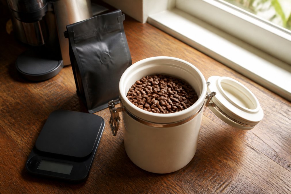 Airtight ceramic canister and bag of gourmet coffee beans on a wooden counter with a digital scale