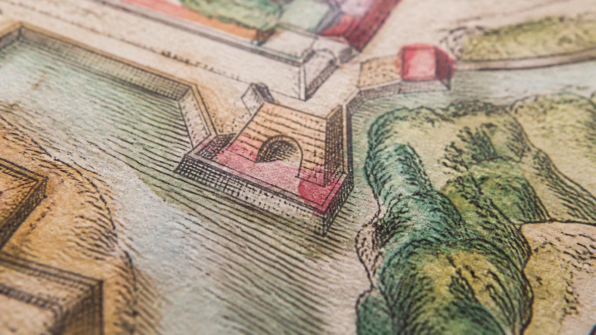 Close-up of an antique hand-coloured engraving showing visible brushstrokes, colour bleeding slightly beyond printed lines, and varying pigment opacity where watercolour has been layered, photographed under natural window light