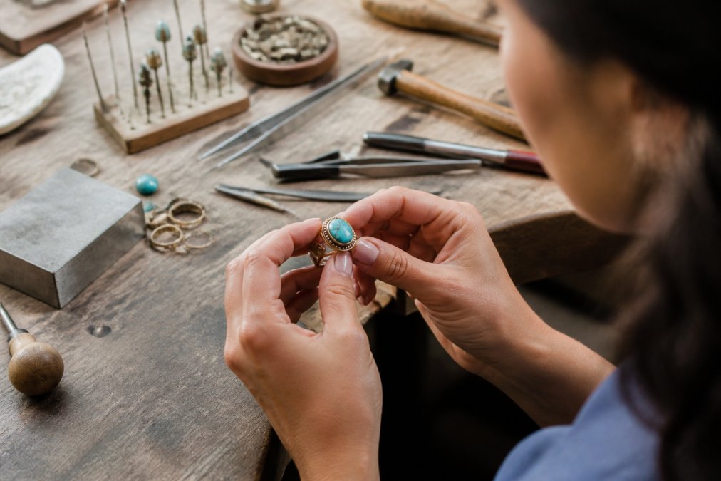Close-up of hands holding a handmade golden bronze ring with a turquoise stone, inspecting the craftsmanship under natural light