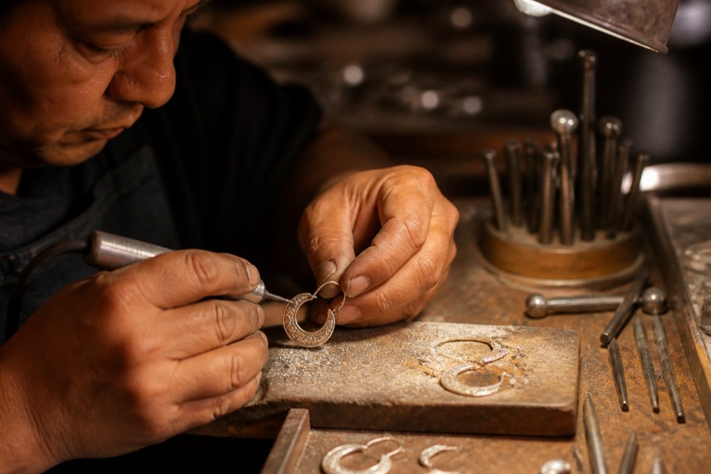 Jeweler using small tools to shape a handmade sterling silver earring on a workbench with metal filings nearby