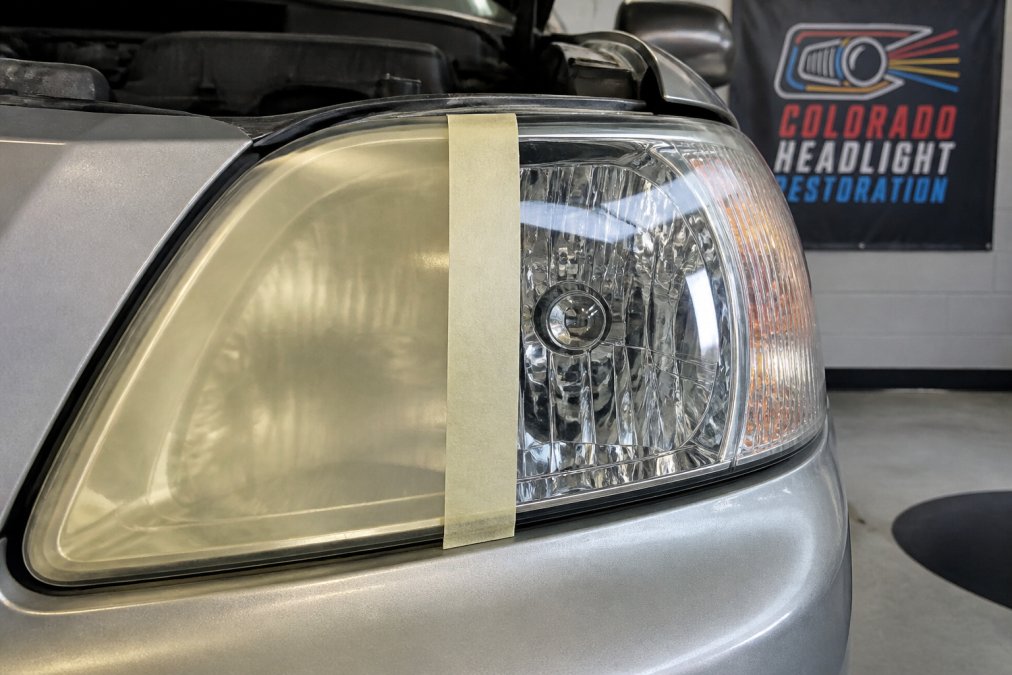 Close-up of a vehicle's headlight showing yellowed, hazy polycarbonate lens on the left side transitioning to a clear, transparent restored lens on the right side, photographed in natural daylight