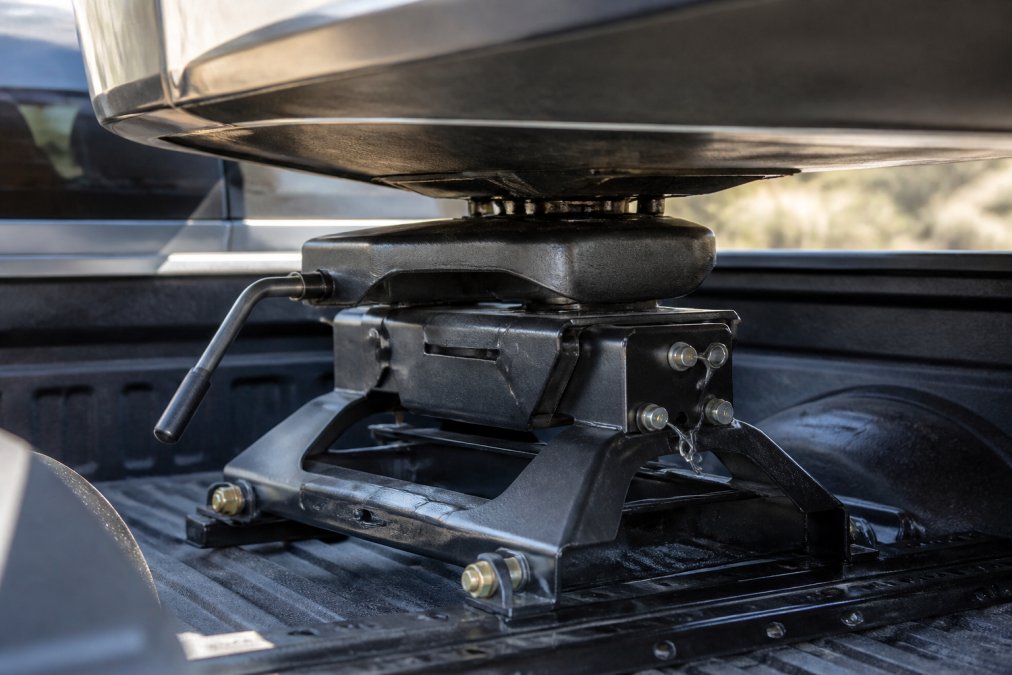 Close-up of a fifth wheel hitch connection mounted securely in truck bed with trailer kingpin engaged, showing heavy-duty coupling mechanism under daylight