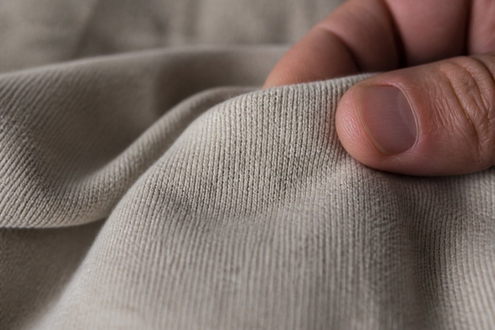 Close-up of heavyweight cotton fabric texture showing tight weave and dense fiber construction, with fingers gently testing the fabric hand-feel