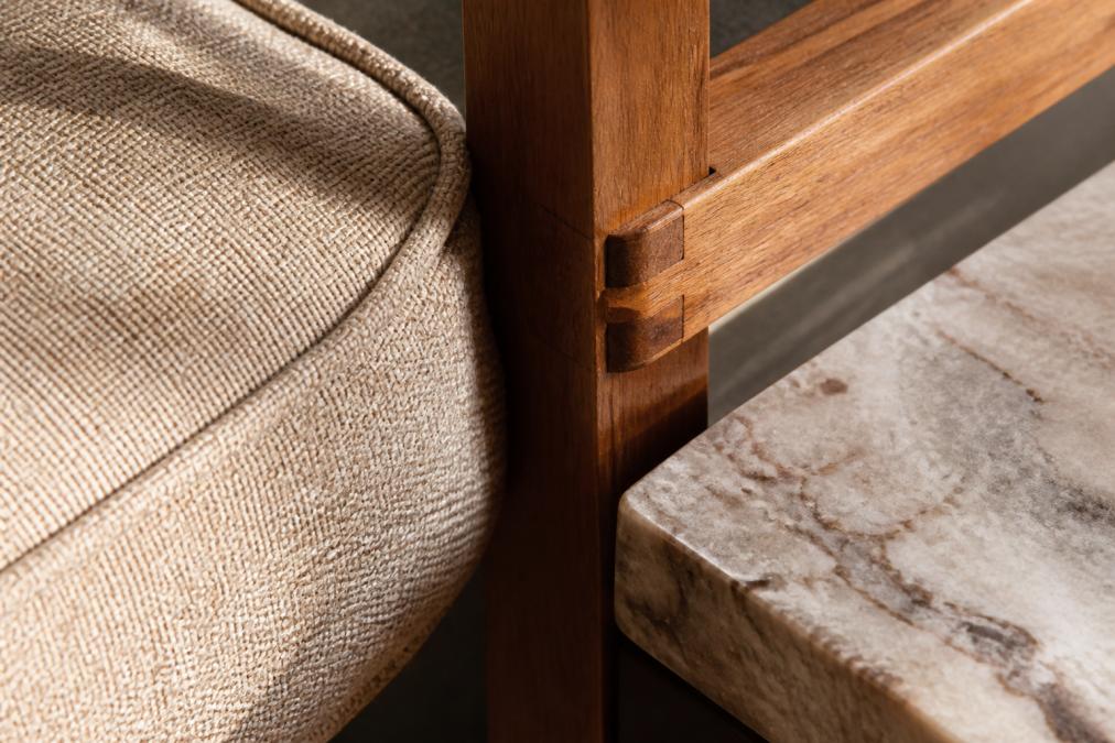 Close-up detail of high-quality upholstery texture showing dense fabric weave, solid wood furniture joint with visible craftsmanship, and polished natural stone surface catching warm light