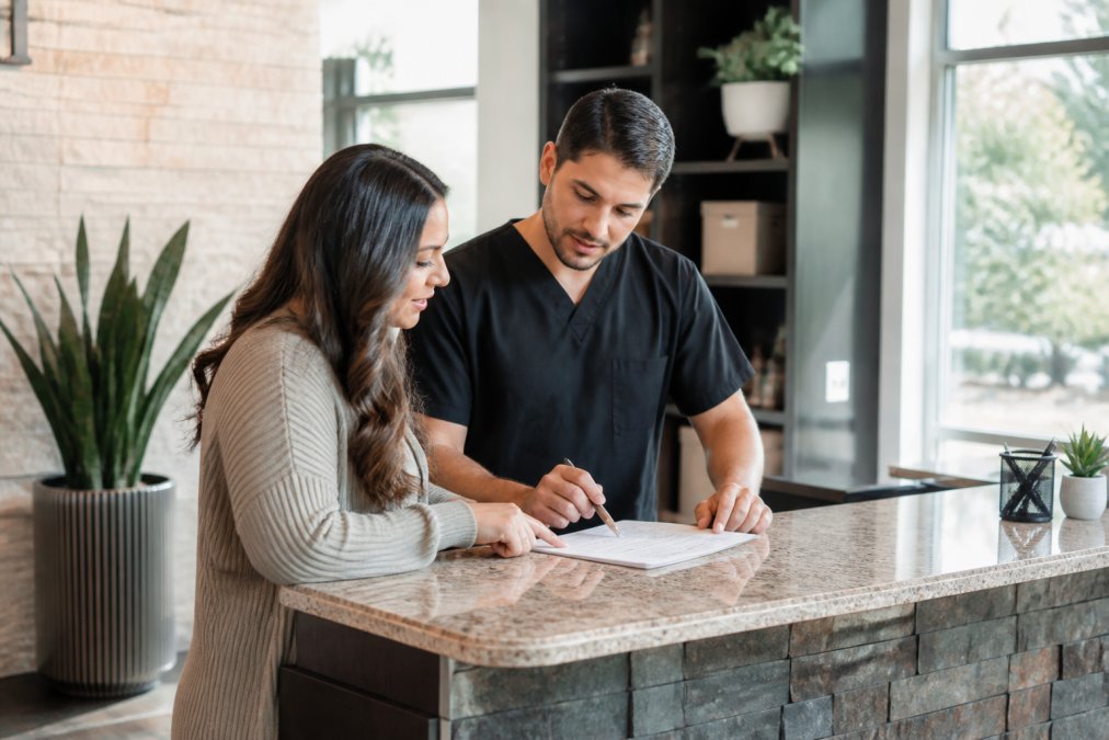 A patient reviewing insurance paperwork with a chiropractor in a bright, welcoming clinic office, both leaning over a document on the front desk