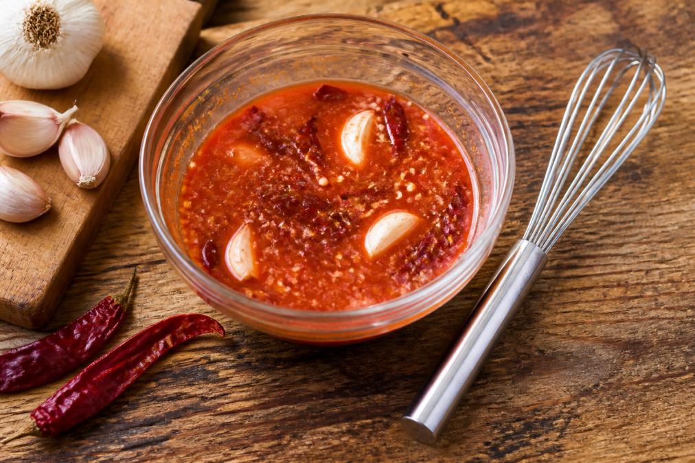 Whisking a vibrant hot sauce marinade with garlic and peppers to show if is hot sauce good for cooking in recipes.
