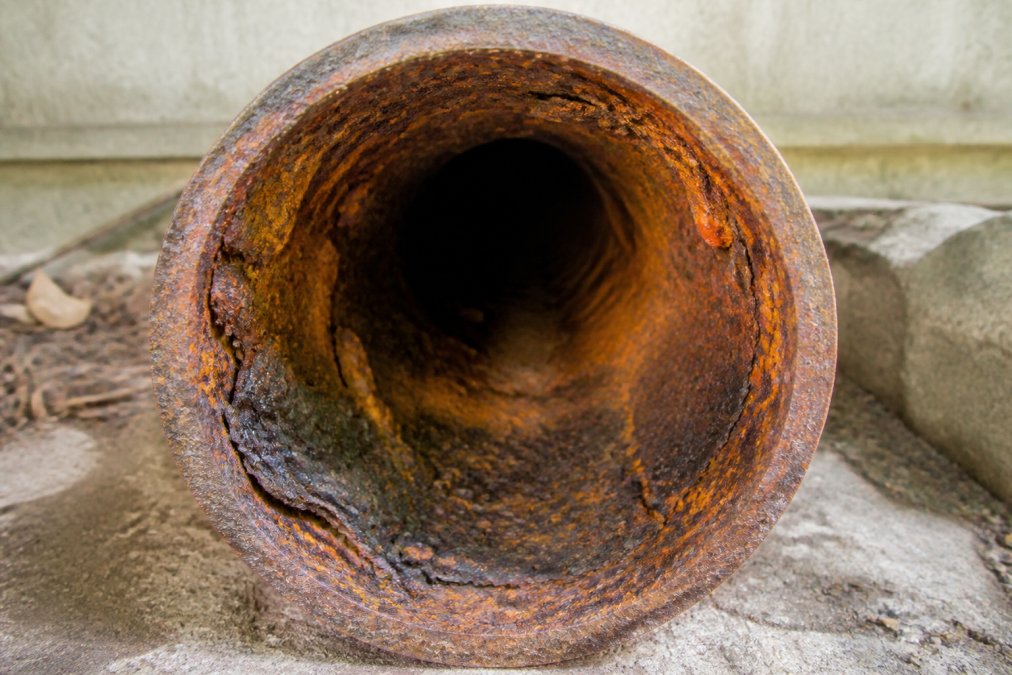Close-up of corroded cast iron sewer pipe showing rust buildup, orange oxidation, and structural wear on interior surface of aged residential property