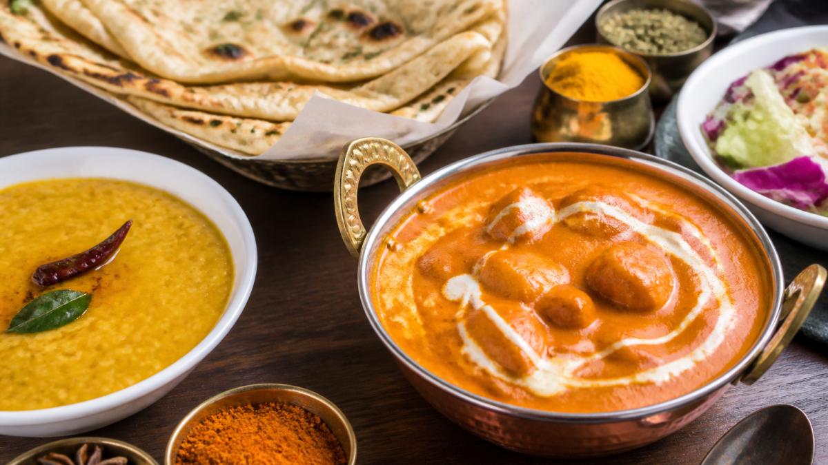 Colorful spread of Indian vegetarian curries including paneer tikka masala, dal, and fresh naan breads arranged on a dining table with vibrant spices and garnishes