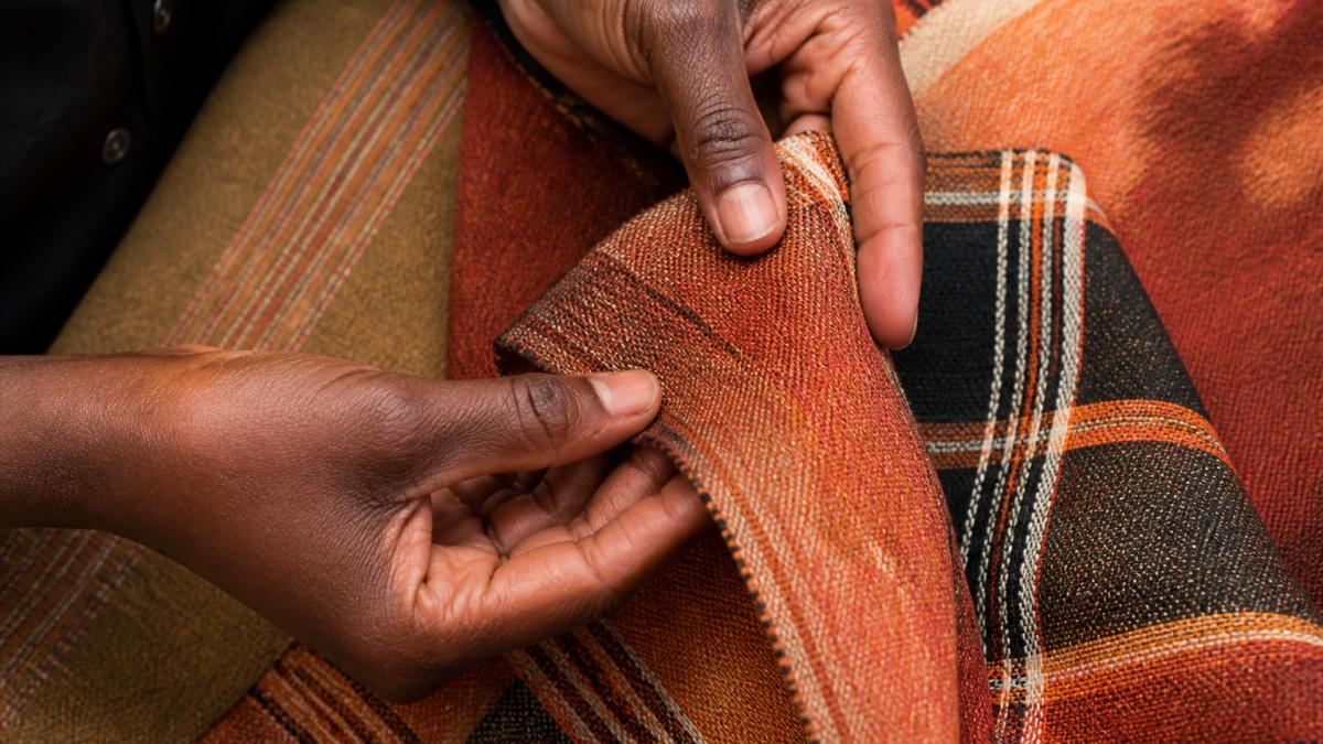 Close-up of hands examining the intricate weave and texture of a vibrant hand-dyed African cotton textile, showing natural color variations and detailed stitching against soft natural light
