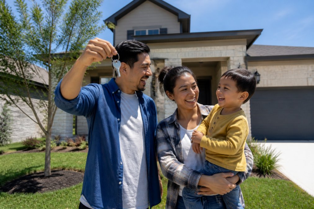 Family standing in front of a new home they're about to purchase, smiling with confidence and relief, with keys in hand and a "Sold" sign visible in the background