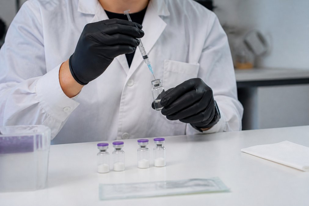Professional demonstrating peptide reconstitution with sterile syringe, bacteriostatic water vial, and peptide vials on clean work surface with proper lighting and organization