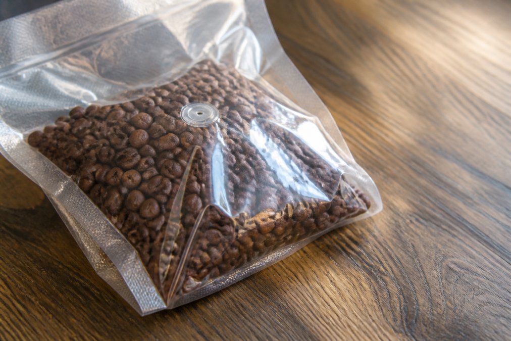 Close-up of freshly roasted whole coffee beans in a vacuum-sealed bag with a visible roast date label, natural lighting highlighting the rich brown bean color and texture