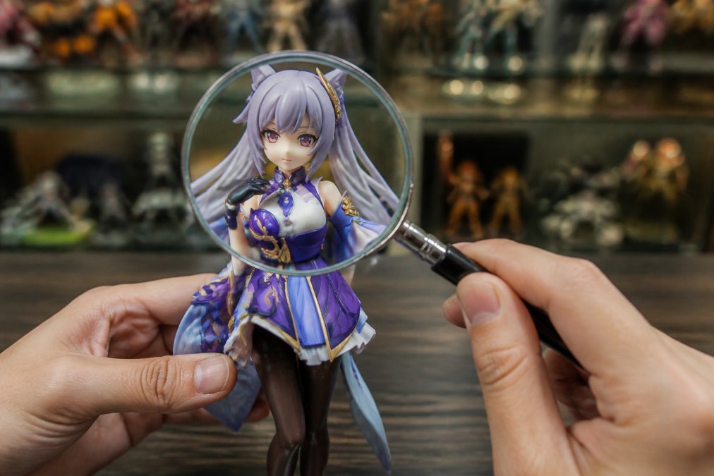 Collector's hands holding a high-end anime figure under bright studio lighting, examining intricate paint details on the face and clothing with a magnifying glass, showing fine sculpting and color gradients