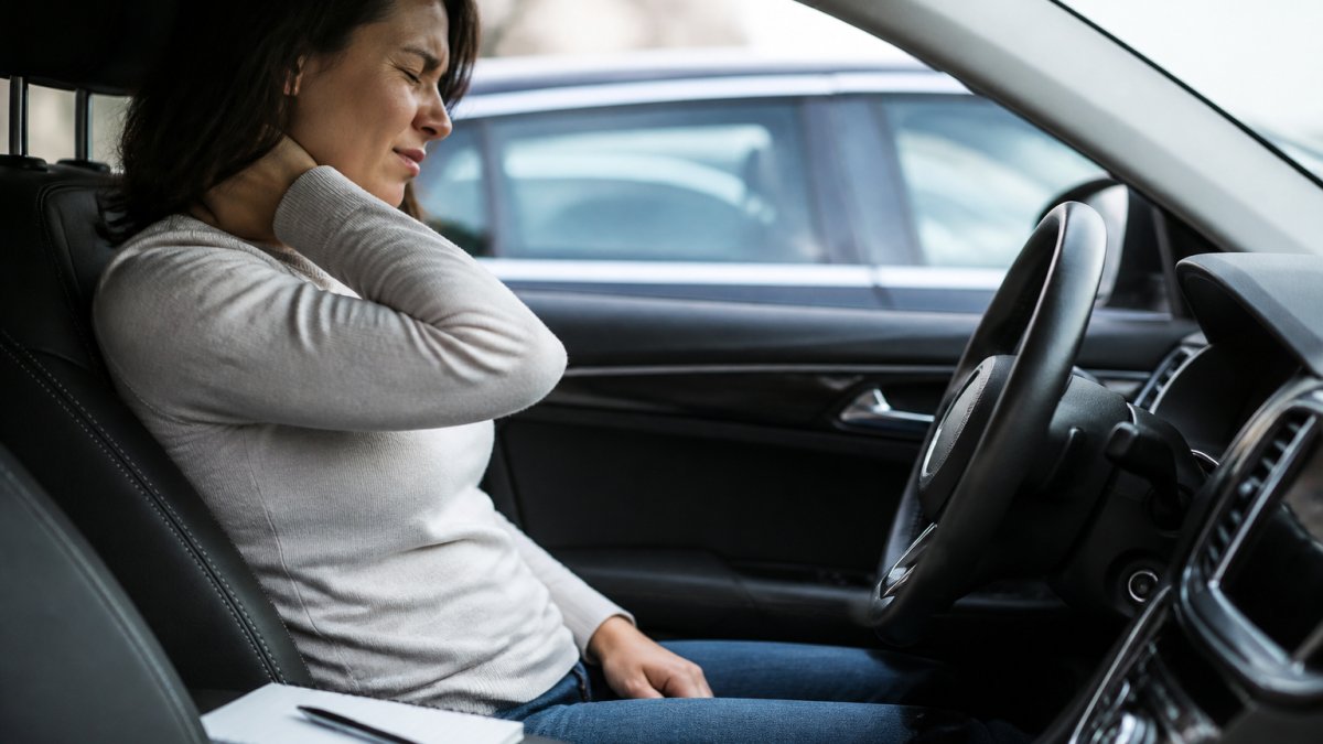 Person sitting in a car clutching their neck in pain while considering if it is worth hiring a lawyer for minor whiplash.
